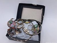 Box containing assorted sterling silver jewelry including rings, bracelets, and pendants with abalone shell and enamel details visible.