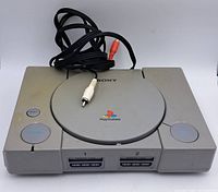 Full view of the PlayStation 1 console top and front with RCA cables on top showing keyboard and disc cover.