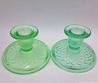 Two uranium glass candle stick holders placed side by side showing their translucent green coloration and patterned bases.