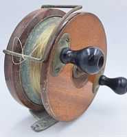 Side angled view of vintage fishing reel showing wooden side plate, black wooden handle, metal frame, and spool wound with clear fishing line.
