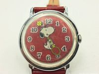 Front view of the watch face showing Snoopy playing tennis on a red dial with silver Arabic numerals and red leather strap.