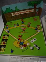 Photo showing the full game board with cartoon characters of Peanuts baseball players, playing pieces, and dice positioned on the field.