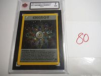Front side view of 2000 Pokémon Team Rocket Rainbow Energy holographic card in protective plastic holder, graded 7 NM by KSA.