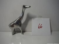 Silver-toned giraffe figurine standing upright, side view, next to paper with number 66