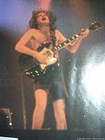 Close-up of a band member playing guitar during performance, shirtless and wearing shorts, capturing the energy of the concert.