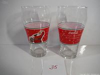 Two clear large glasses with red Coca-Cola holiday bands shown front and back featuring Santa Claus and holiday text.