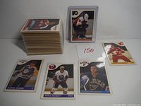 Stack of approximately 120 sleeved hockey cards and five individual hockey cards laid out, showing players Marcel Dionne, Mike Bossy, Doug Gilmour, and one unidentified player in Calgary Flames uniform.