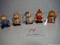Five vintage hollow soft plastic Garfield key chains displayed in a row showing various themed outfits. One is missing the key chain attachment.