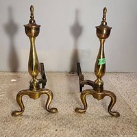 Front view of the pair of brass andirons showing height, shape, and finial tops