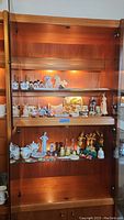 Display of items on three wood shelves including animal figurines, snowmen, decorative plates, and various small collectibles.