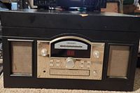 Front view of black Crosley record player showing speakers, control panel, and chip damage on top edge.