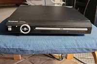 Front view of Curtis DVD player showing full unit on blue cloth surface, disc tray and power button visible.