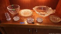 Display of eight various glass and crystal items on wooden shelf, including bowls, plates, candle holders and salt shaker