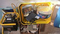 Three boxes with assorted electrical and household items including a yellow work light, transformer, and accessories