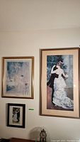 Photo showing two framed art prints hung side by side on a white wall. One smaller print below them partially visible.