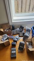 All batteries and boxes spread out on a table near a window, some batteries wrapped in bubble wrap, some in boxes, plastic basket nearby.
