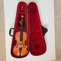 Violin inside open red velvet-lined hard case with bow secured above it