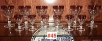 Full view of two sets of stemware showing 7 larger and 7 smaller glasses with ruby red bowls and gold decorative banding