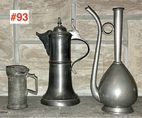 Overview of all three vintage pewter pieces against a stone wall background: ewer, tankard, and small measure side by side.
