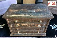 Front view of four-drawer spool cabinet showing carved panels, painted advertising text and varied knobs