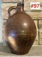 Front view of the large brown antique Dutch earthenware jug with handle and narrow neck, resting on a stone surface.