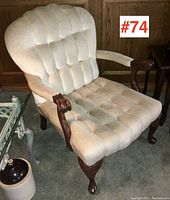 Side angle view of the armchair showing the tufted back and seat upholstery, and carved wooden armrest and legs.