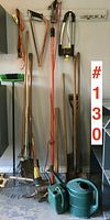Full view of all gardening tools including rakes, shovels, saws, watering cans hanging and standing against the wall.