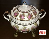 Front and side view of porcelain tureen with lid on brass trivet showing the colorful romantic scene decals and gold trim.