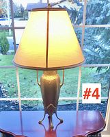 Full view of the brass table lamp standing on a wooden table with the fabric shade illuminated, showing the lamp height and shade diameter.