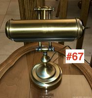 Brass desk lamp with adjustable horizontal cylindrical shade and round stepped base shown on wooden surface.