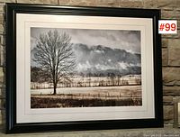 Full view of the framed landscape print hung against stone wall, showing black frame and white matting