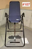 Front view of the inversion table showing the blue padded backrest, black frame, and ankle supports on light-colored flooring.