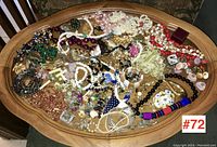Full view of large lot of mixed vintage costume jewellery on wooden table, showing wide variety of necklaces, bracelets, earrings, and brooches in various colors and styles.