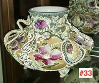 Front angle view of Nippon moriage porcelain vase showing detailed raised slip floral decoration and decorative handles, sitting on small feet.