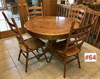 Round oak dining table with 4 ladder-back chairs viewed from an angle showing table top and pedestal base, placed on tiled floor near double glass doors.