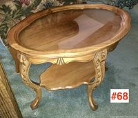Full view of oval side table with glass insert showing carved legs and lower shelf.