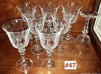 Seven crystal wine glasses displayed on wooden shelf, one upside down glass is chipped on the rim.