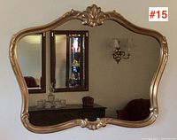 Front view of large rectangular vintage mirror with curved edges and gilded frame hanging on a wall, showing reflective surface and interior background.