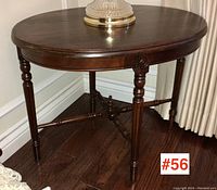 Vintage dark wood oval side table with turned legs and stretcher, shown from an angle with a lamp on top.