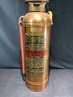 Front view showing copper cylinder, brass label plate with embossed Empire branding and usage instructions in red and gold letters, and red hose attached to side.