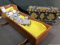 Photo showing pine doll bed with crocheted yellow blanket and three small cloth dolls (boy, girl, cat).