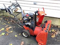 Side view of red Ariens snow blower showing engine, handle, wheels and intake housing