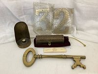Photo showing the brass frankincense and myrrh chest on a velvet base, large brass key in front, two bubble wrapped brass house numbers, and a brass candle holder near left side.