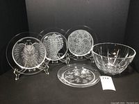 Five-piece set: four Lalique collector plates and one large lead crystal bowl displayed on black background.