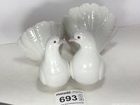 Full view of white glossy porcelain figurine showing two doves with spread tail feathers facing each other touching beaks.