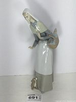 Front angle of glazed porcelain Lladro shepherdess figurine with bread basket and puppy at her feet