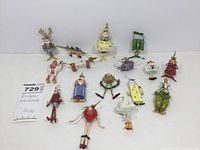 Photo showing all 16 Krinkles mini tree ornaments laid out on a white background, showcasing the variety of figures including animals, pastry-themed figures, and decorative characters with feet and whimsical faces.