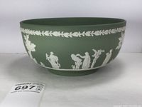 Full side view of the sage green Wedgwood Jasperware bowl showing white relief of classical figures, tree, and leaf garland around rim.