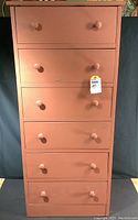 Front view of the wood chest of drawers showing six drawers with round knobs, painted reddish-pink, some paint imperfections visible.