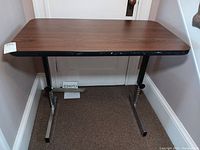 Side view of adjustable height table showing wood grain top and metal base with signs of wear.